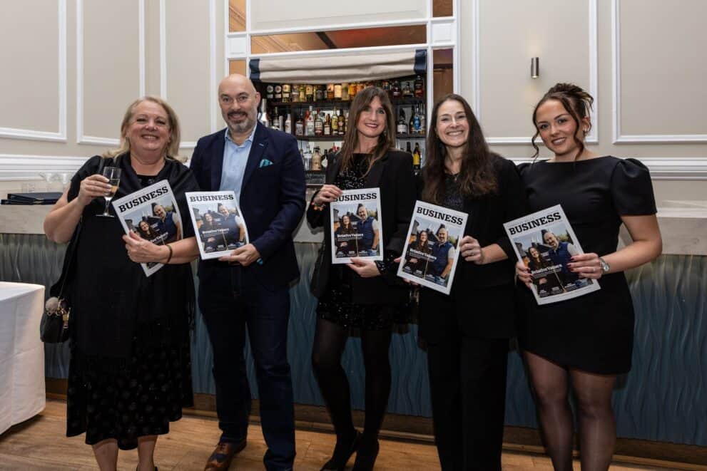 Group of five professionals holding business magazines at a networking event.