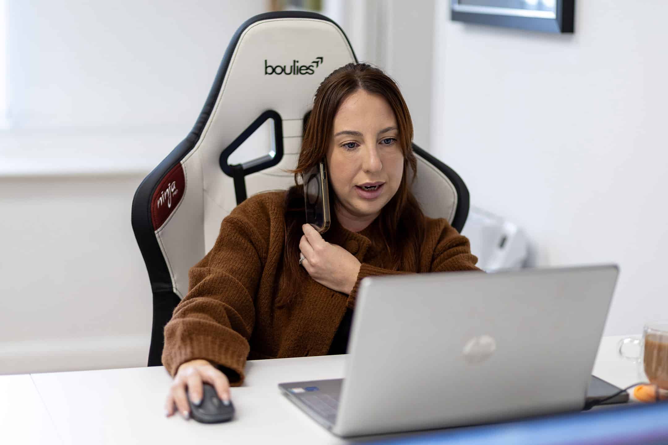 Woman working at desk with laptop and headset in office.