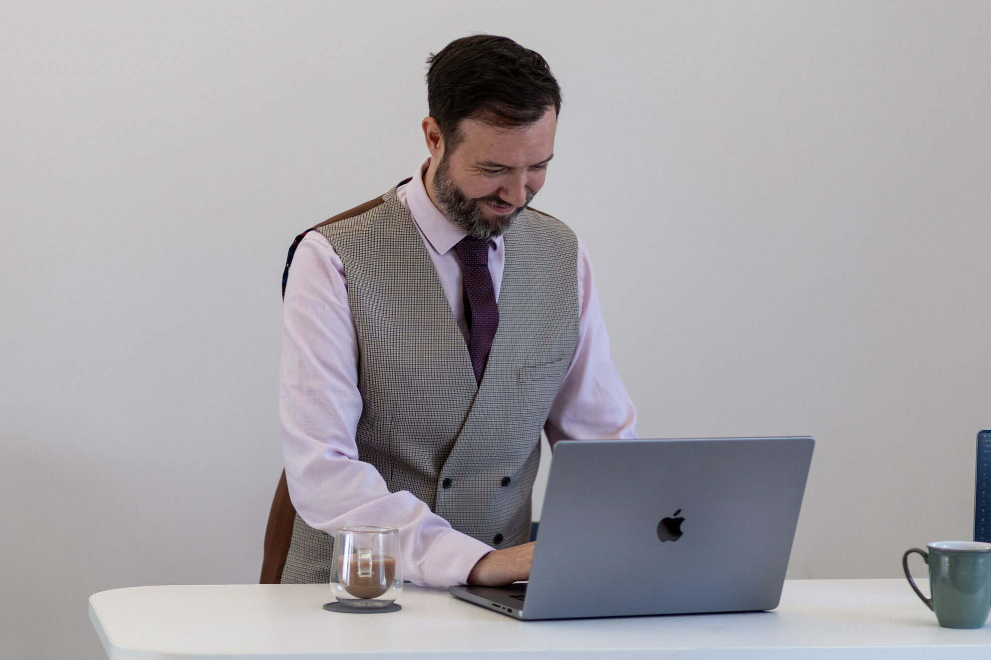 Man working on a laptop at a desk with a glass of water and a mug.