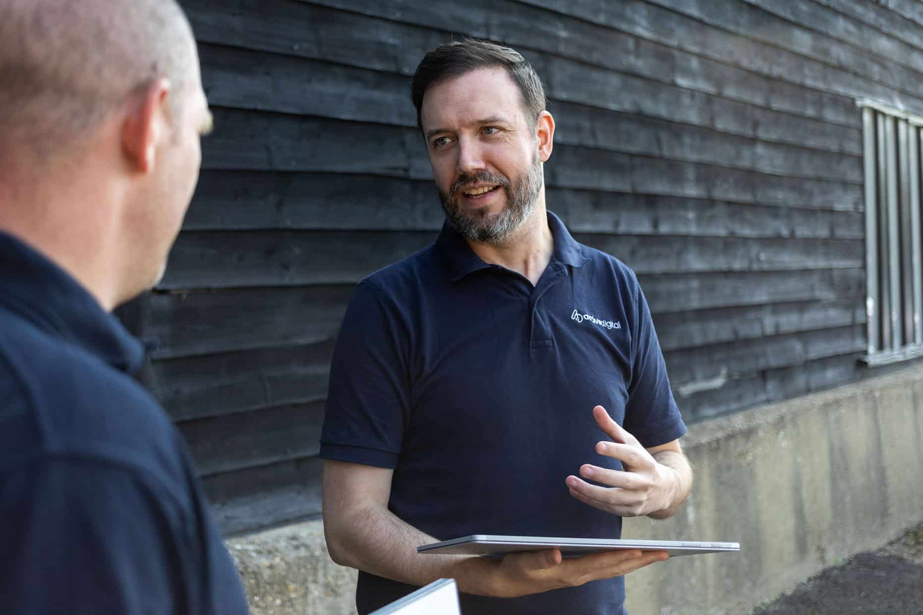 Two men having a conversation outdoors, one holding a tablet.