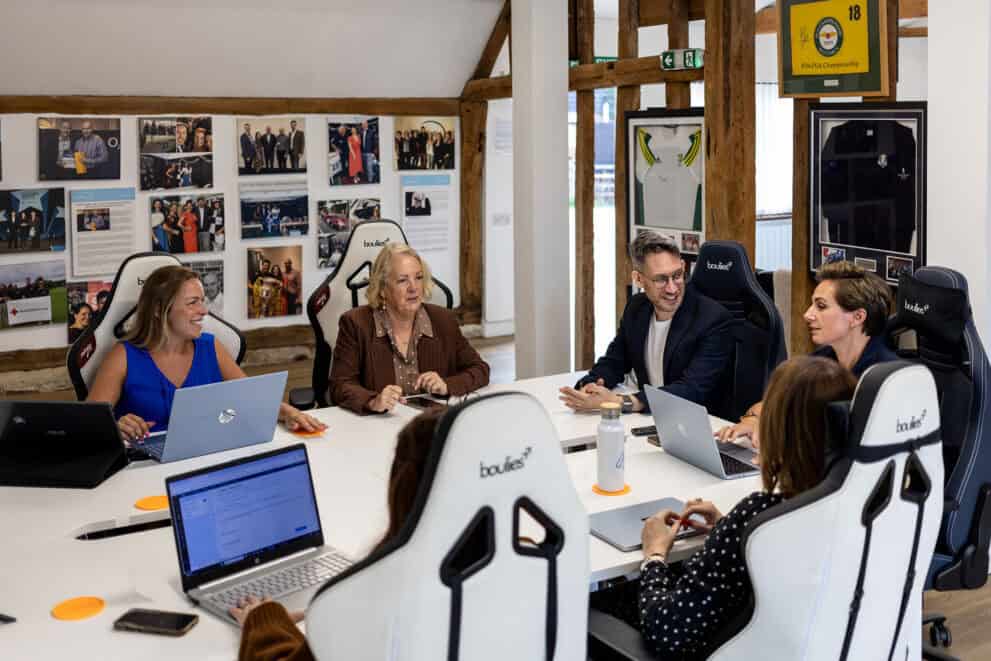 Group of professionals in a meeting room with laptops and presentation screens.