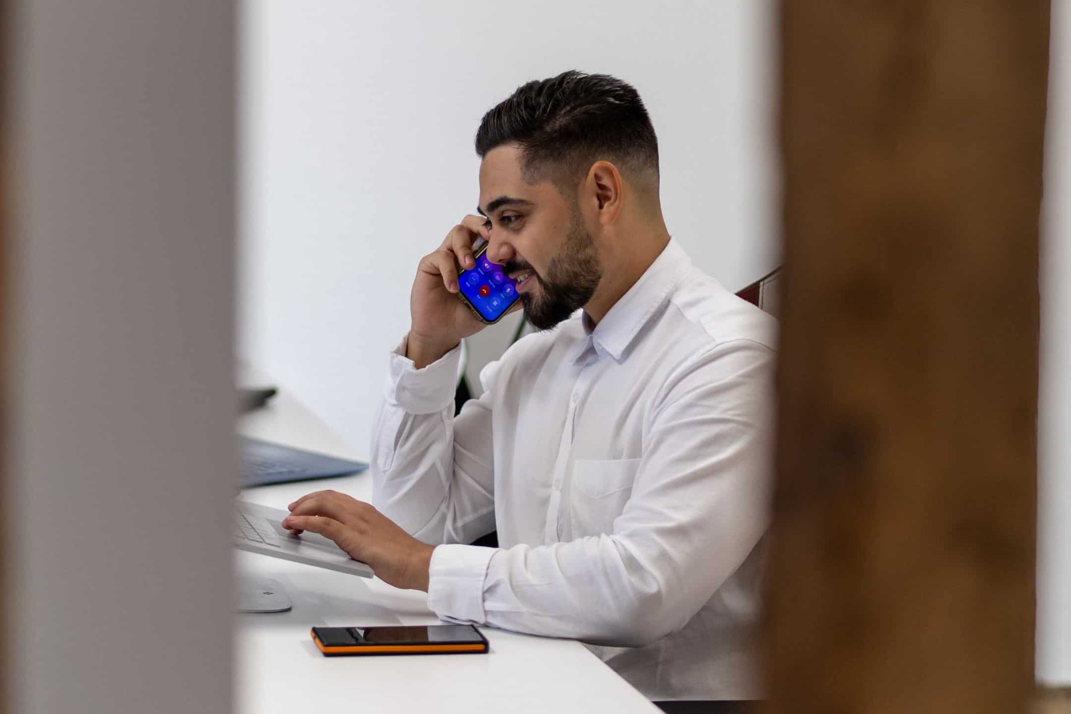 Man in white shirt talking on a mobile phone in an office setting.