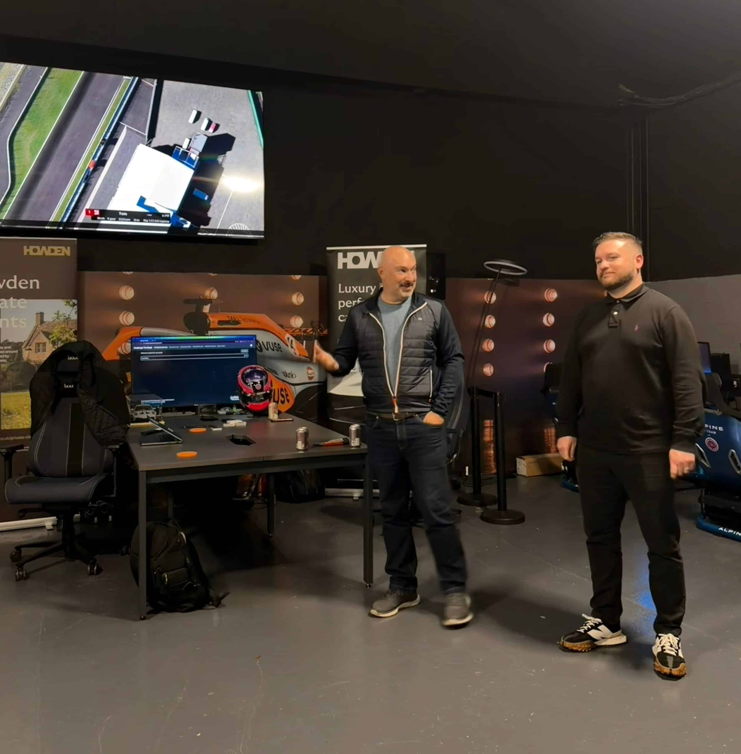 Two men standing in a room with racing simulation equipment and screens.