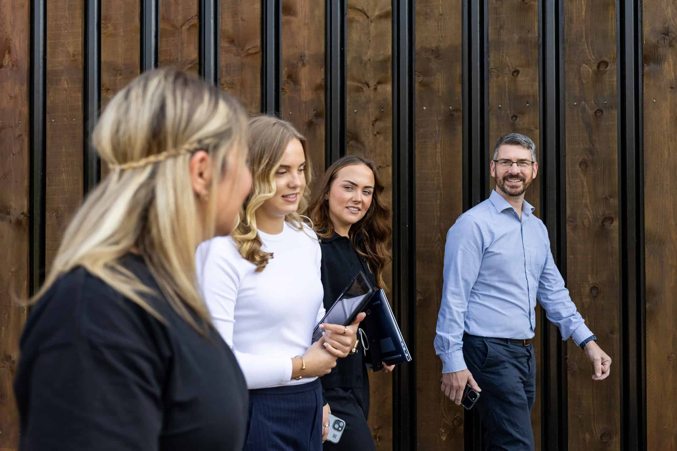 Group of professionals standing outside near wooden wall.