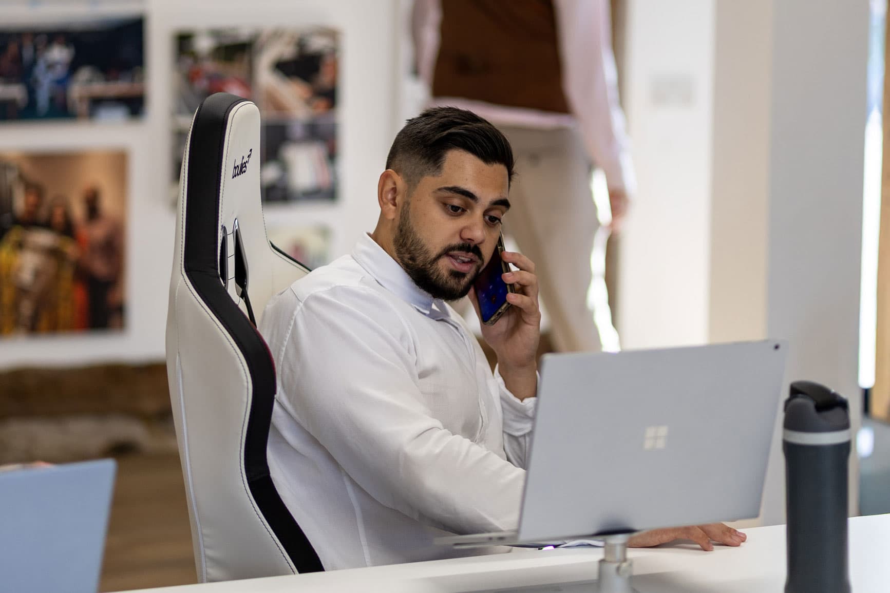 Man working on laptop and talking on mobile phone in office.