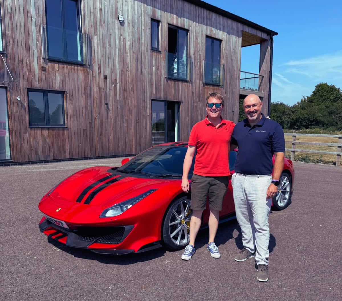 Red sports car with two men standing beside it outside a modern building.