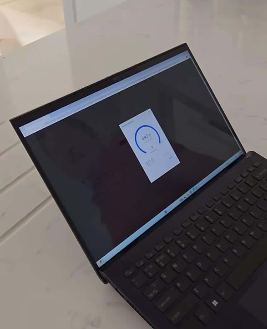 Laptop showing network speed test results on screen in a modern office setting.