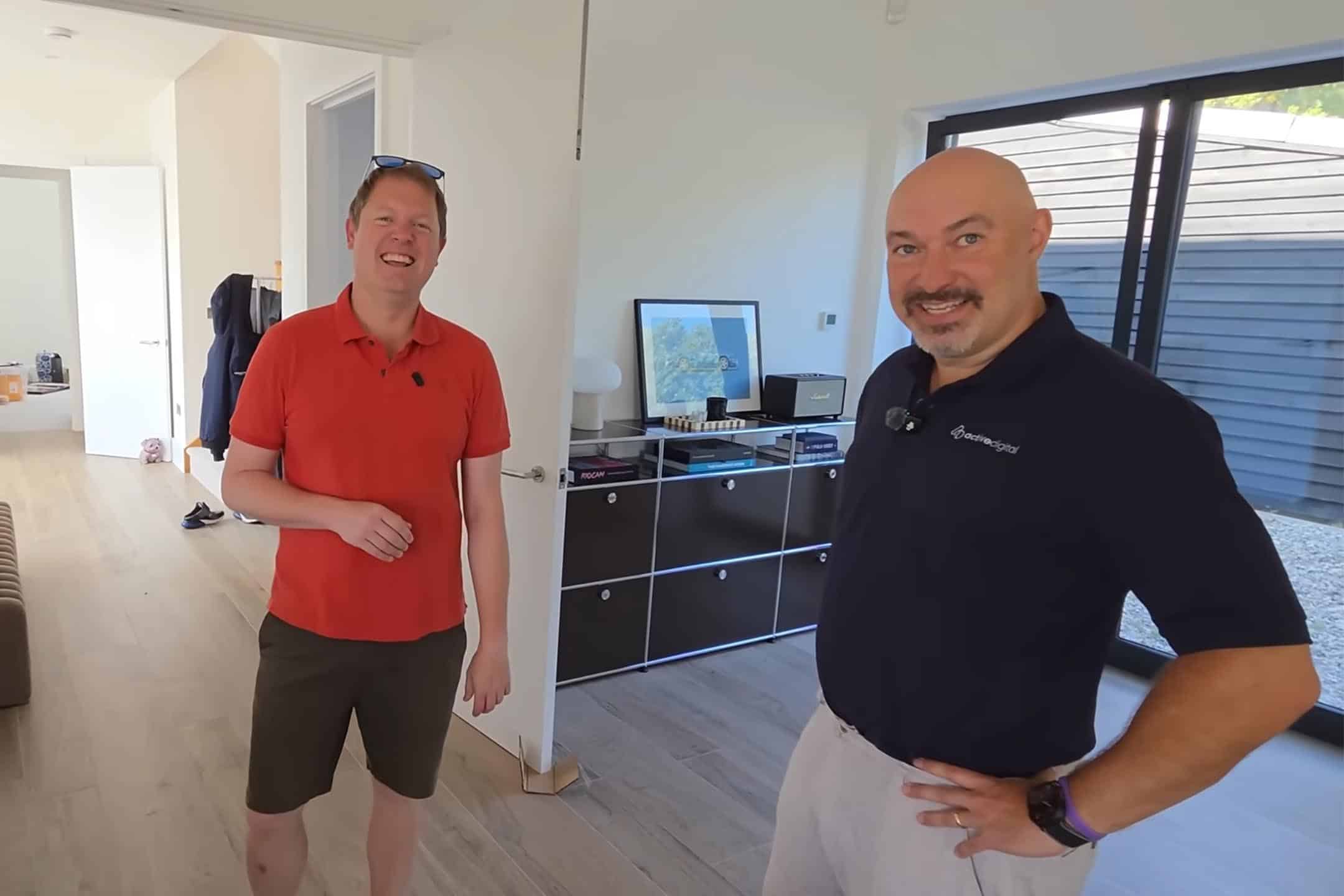 Two men smiling in a modern office with a computer and large window.
