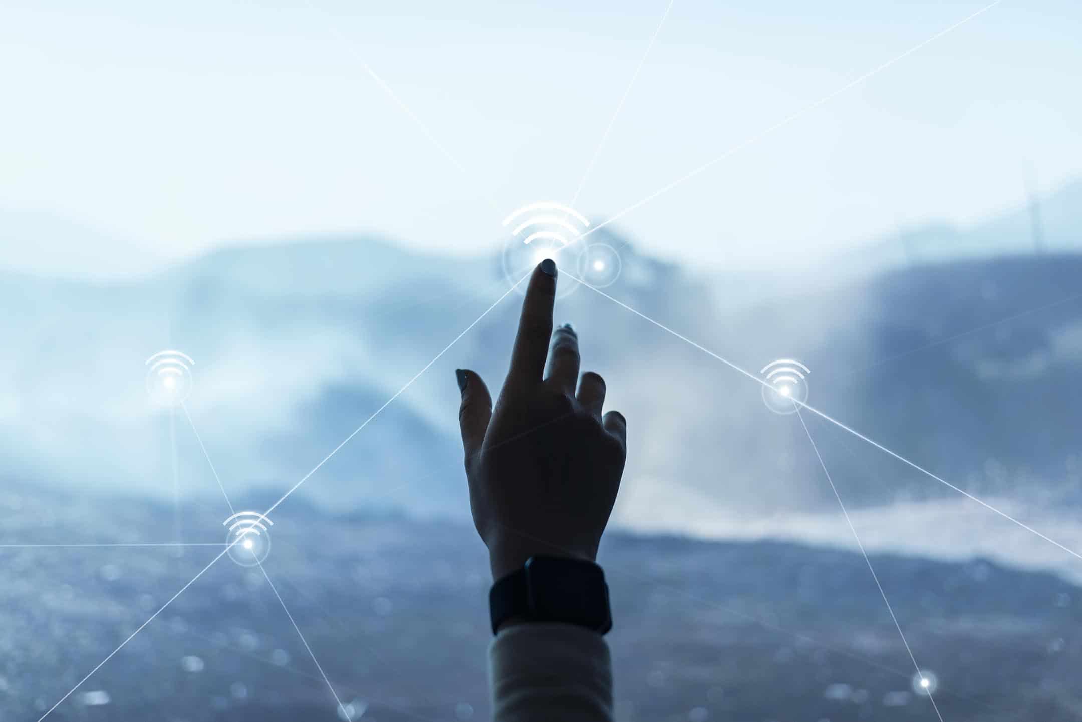 Hand touching a digital network interface with a mountain background.