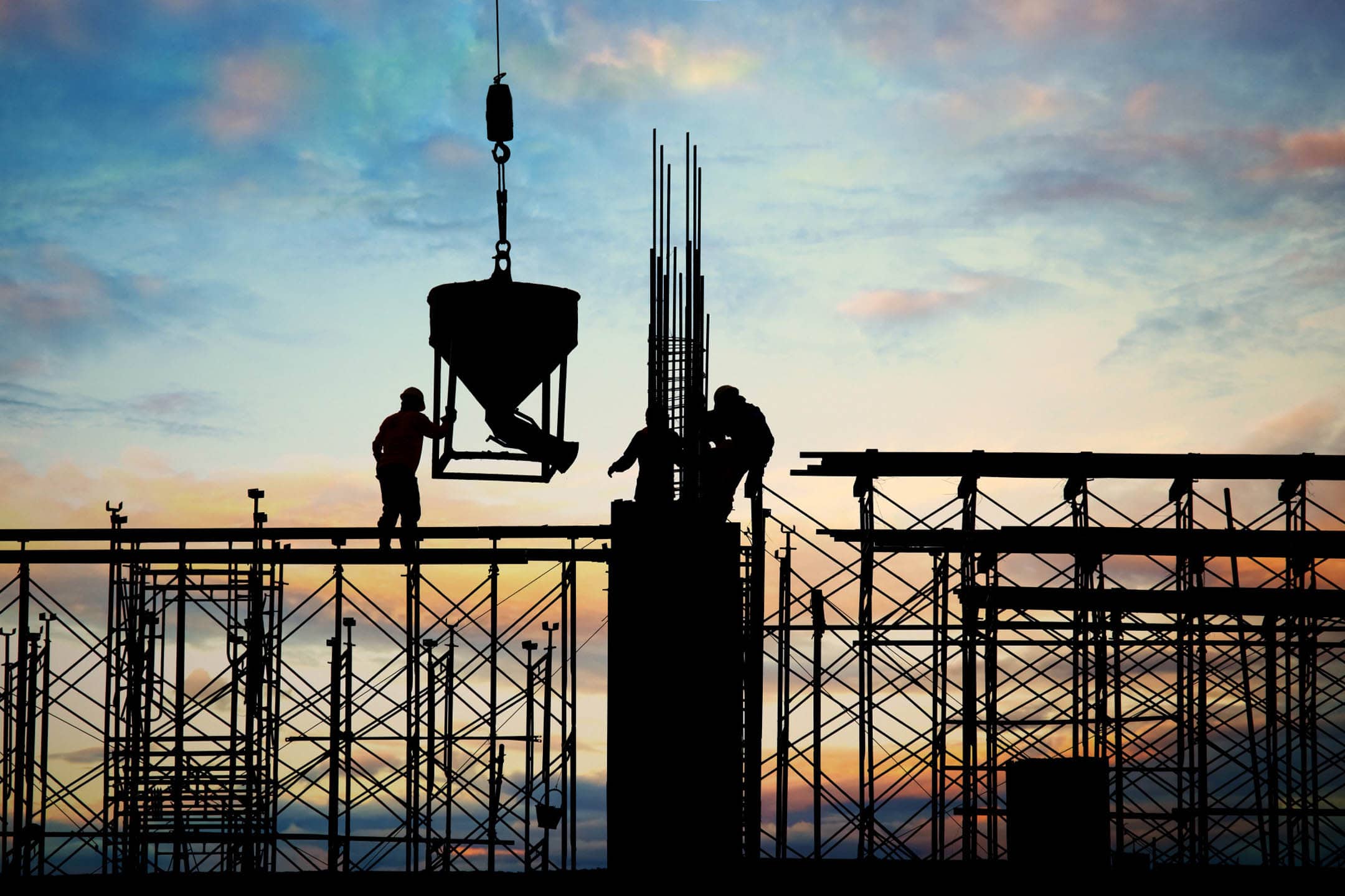 Workers installing steel framework on a building at sunset.