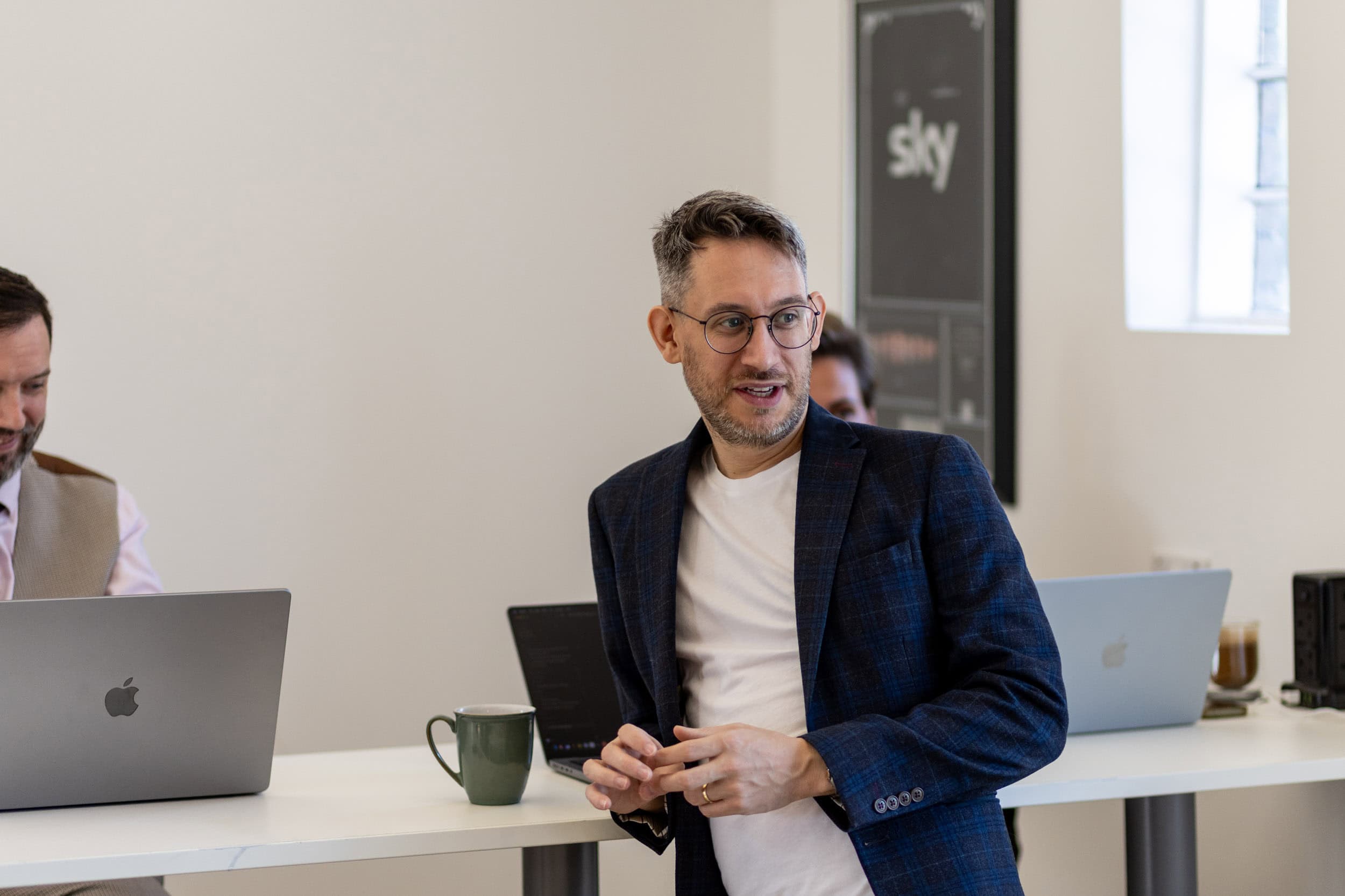 Man in business attire speaking during a meeting in a bright office.