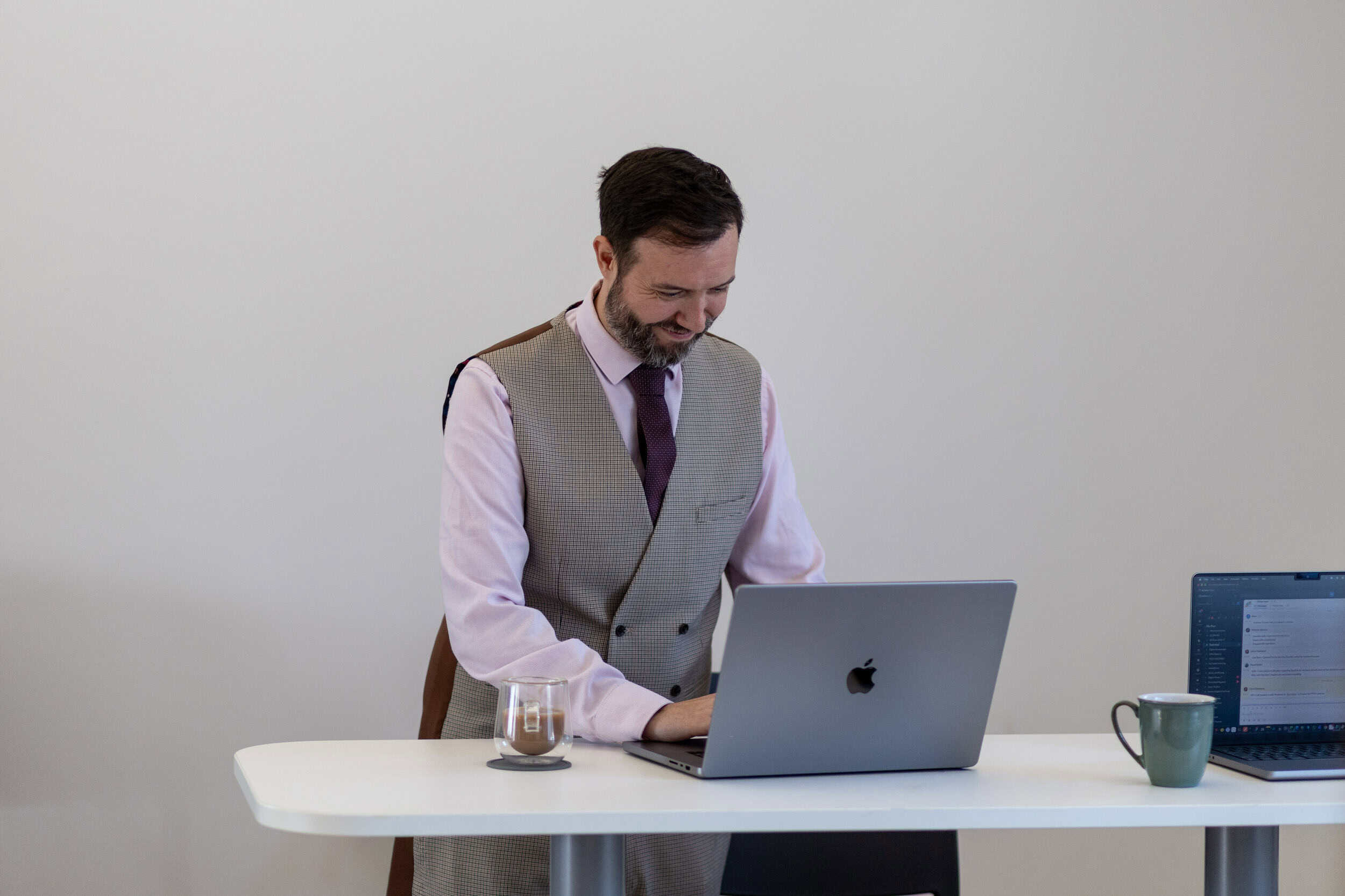 Man working on laptop at desk with coffee mug in modern office.