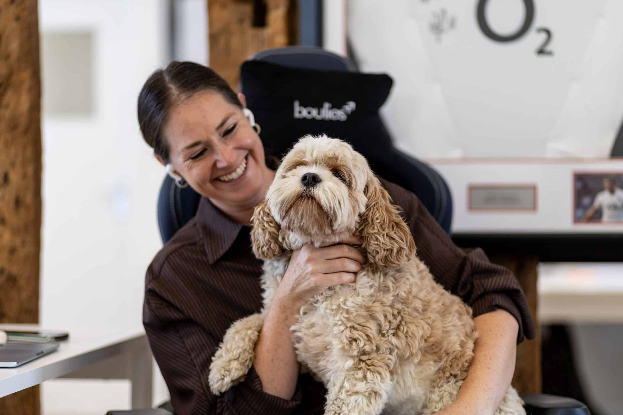 Woman smiling with a fluffy dog in an office environment.