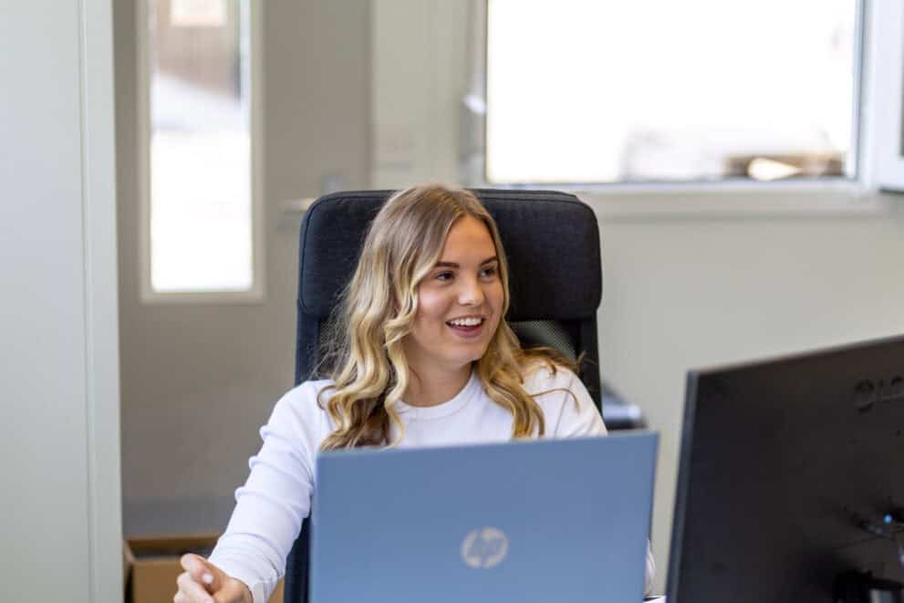 Young woman with blonde hair working on a laptop in an office.